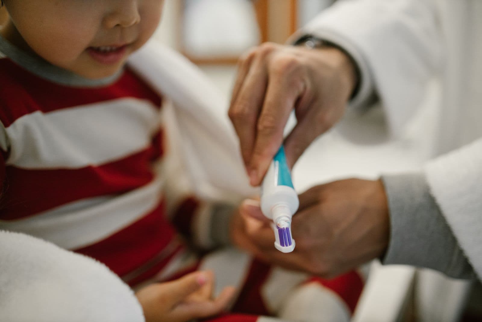 Parent adding toothpaste to a child's toothbrush for daily dental care