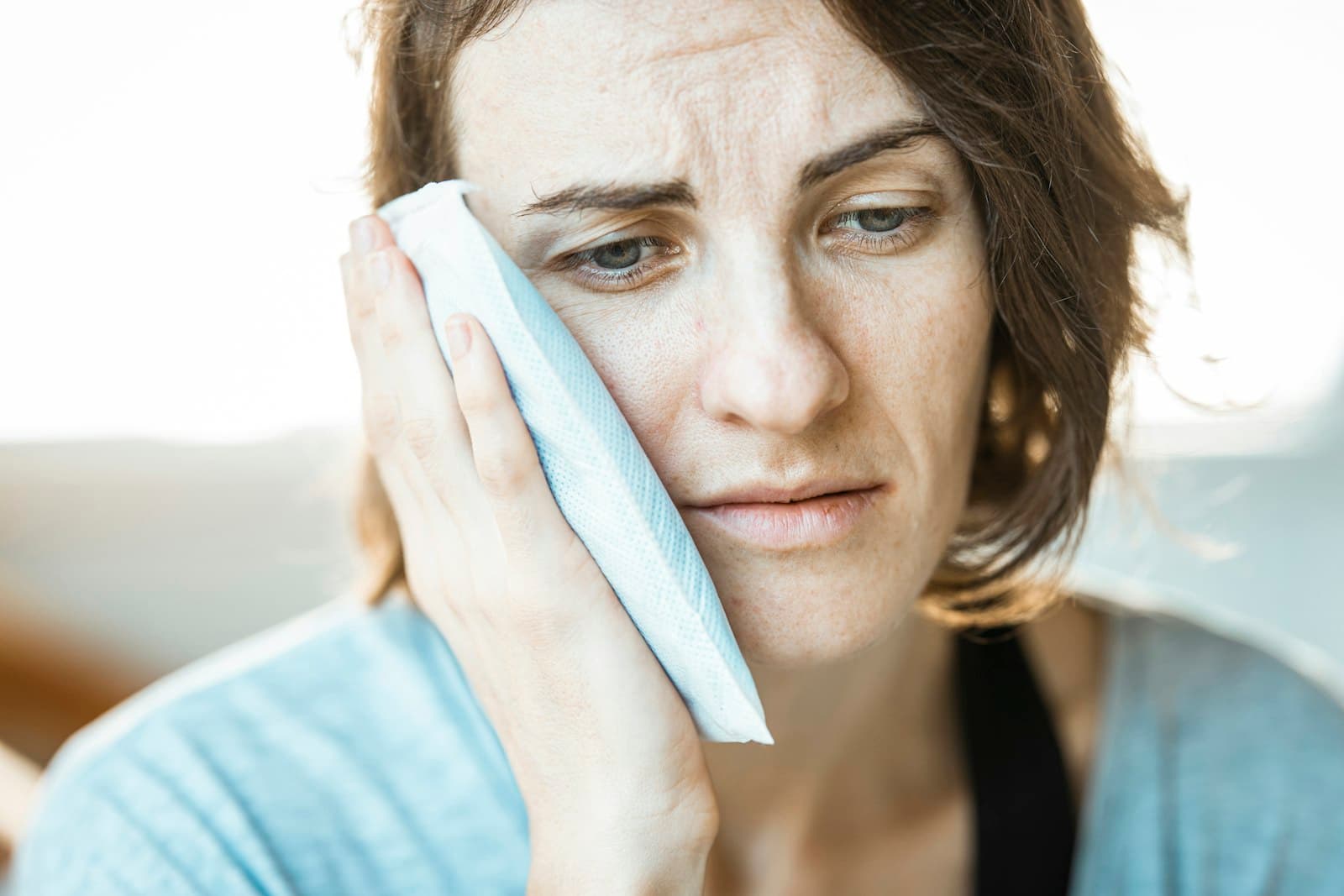 Woman holding a cloth to her cheek while recovering from a dental procedure